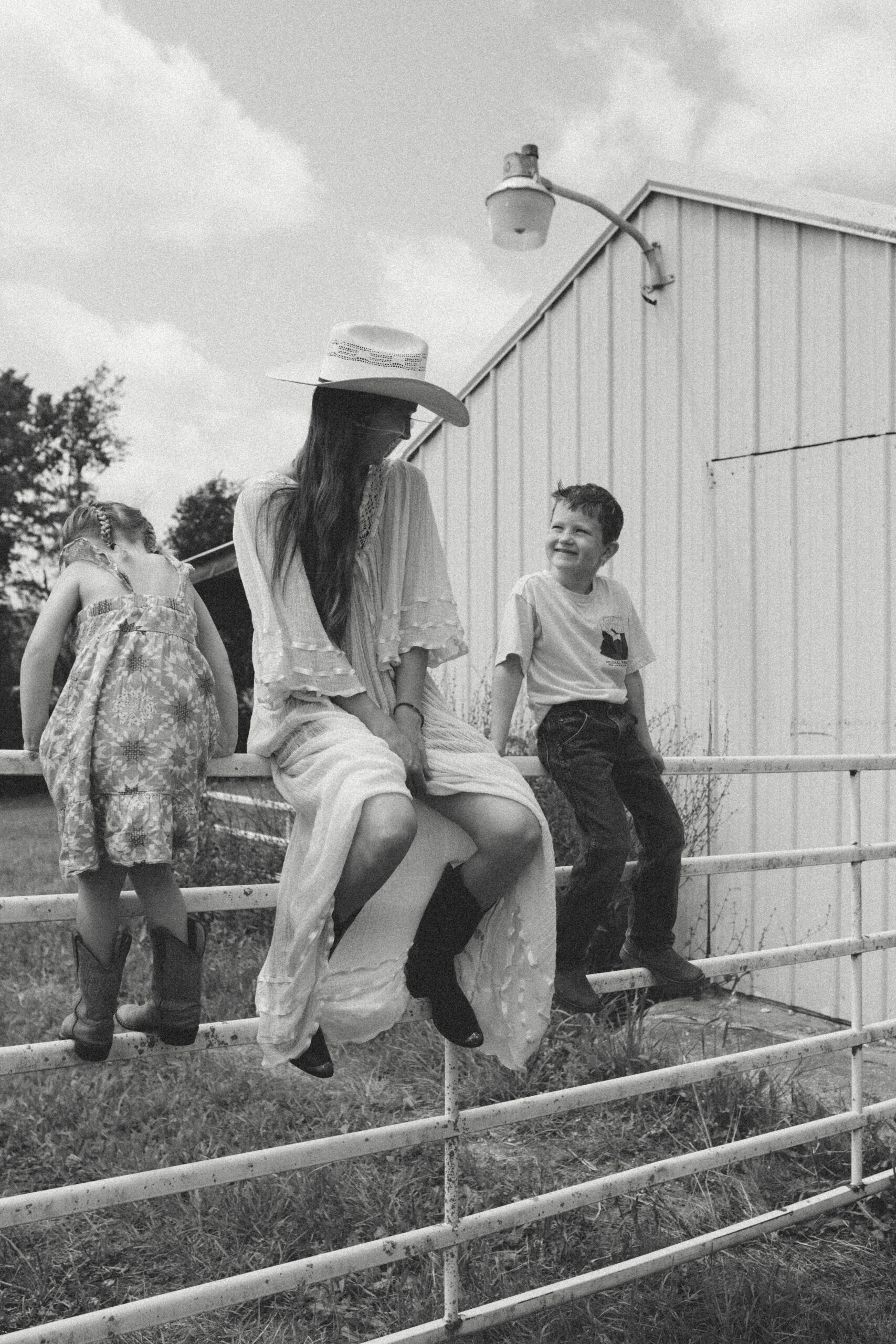 mom looks over at son while sitting on fence rail. son looks to her and smiles during editorial family session in saint louis missouri