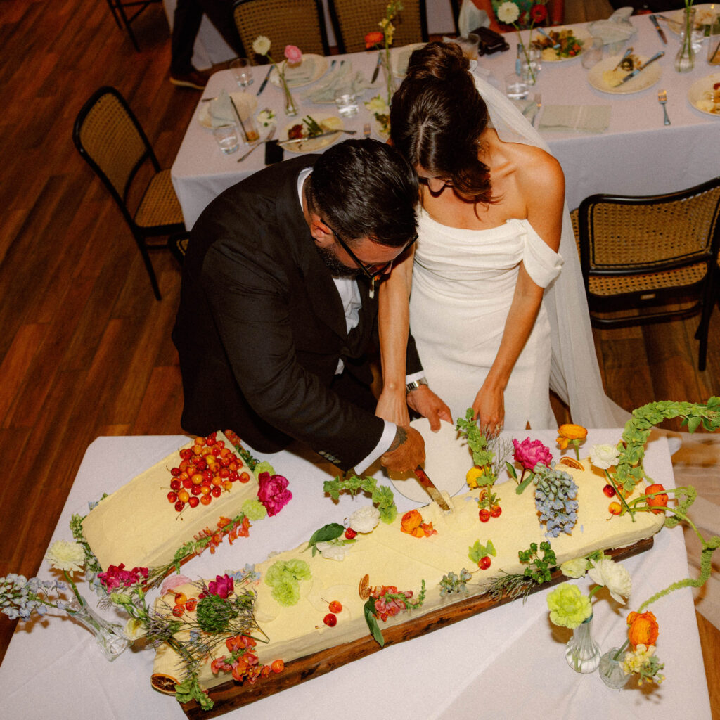 bride and groom cut into their wedding cake during a loose-editorial wedding reception