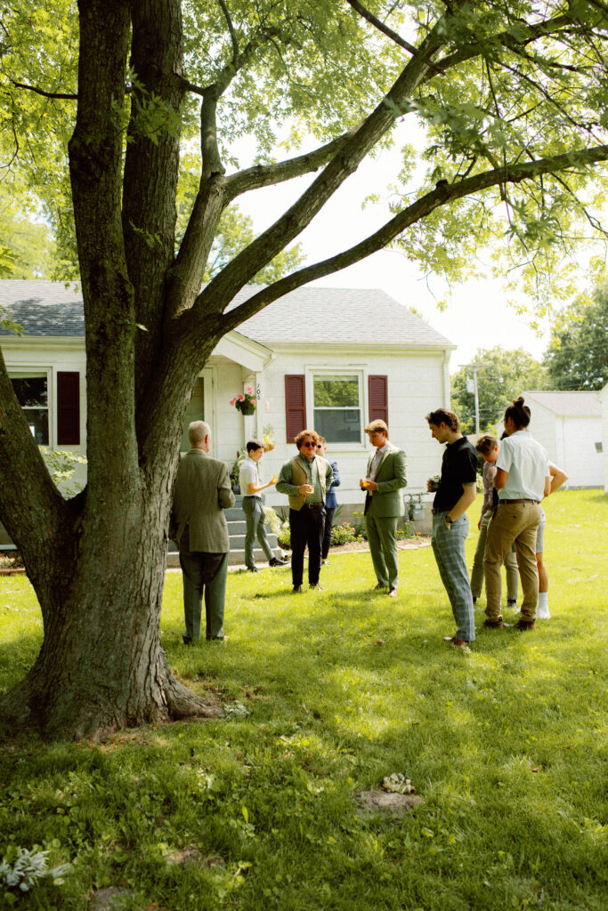 groomsmen stand in front of grooms house while getting ready during elevated backyard wedding in columbia mo