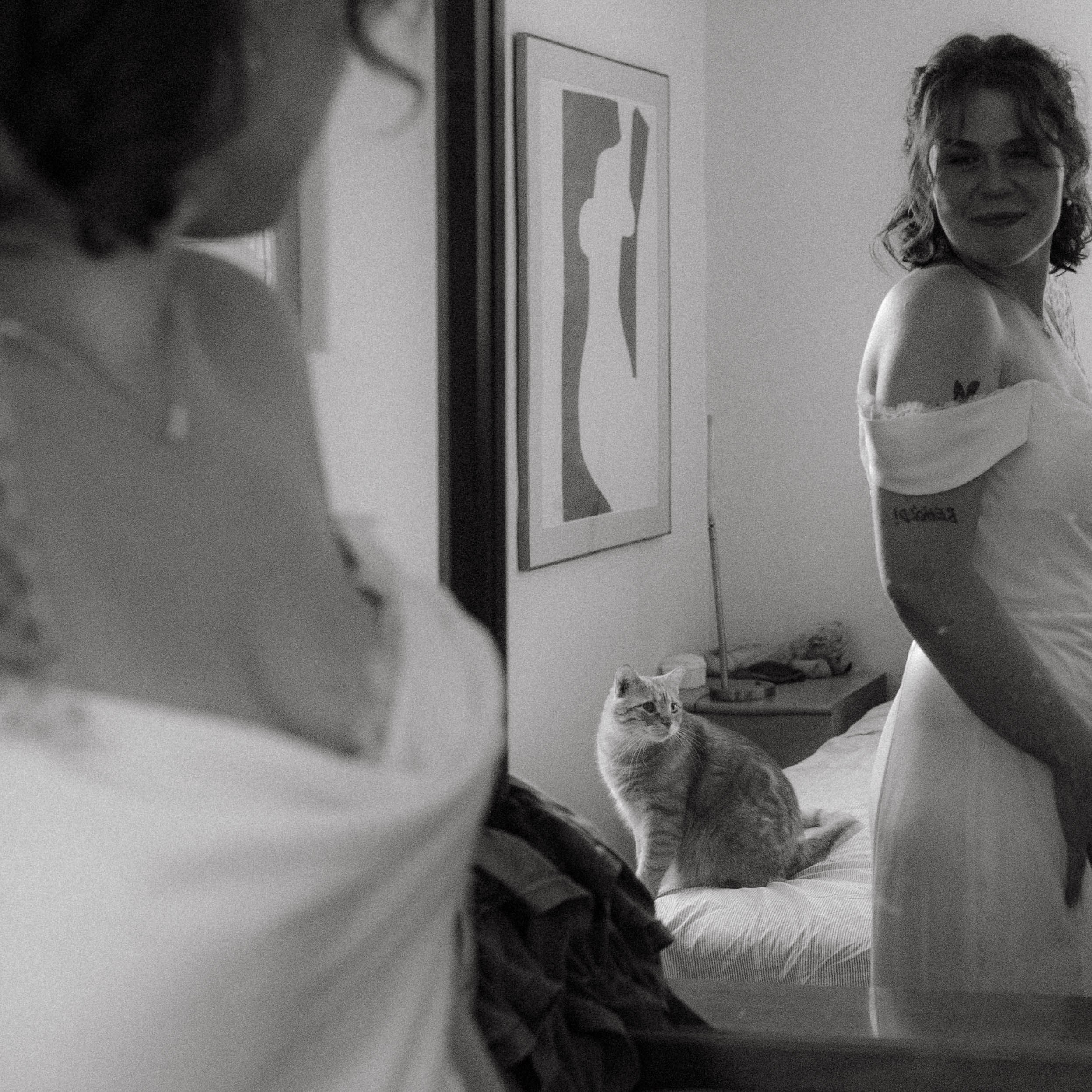 bride looks in bedroom mirror as her cat sits on her bed during columbia mo backyard wedding