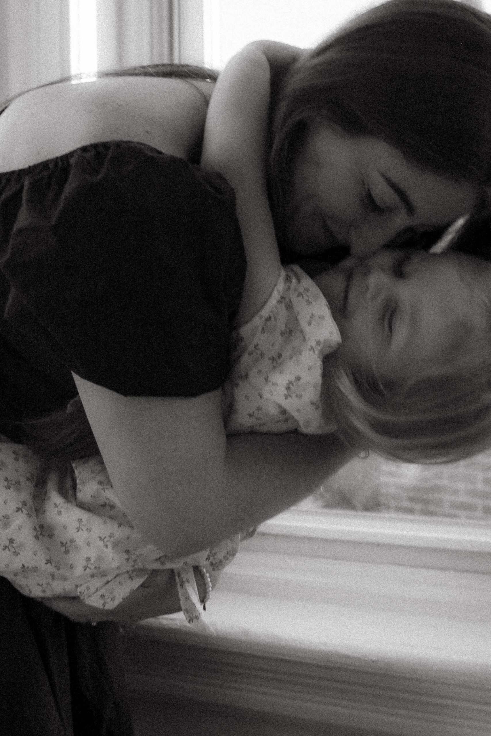 Black and white documentary-style photo of a mother holding her daughter and smiling, captured during a luxury in-home family photography session in Chicago. Emotional, candid moment highlighting genuine connection and timeless storytelling for families who value artistic, relaxed family portraits.