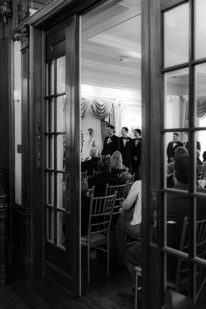 loose mansion wedding ceremony shot through french doors black and white; presence forward documentary photography