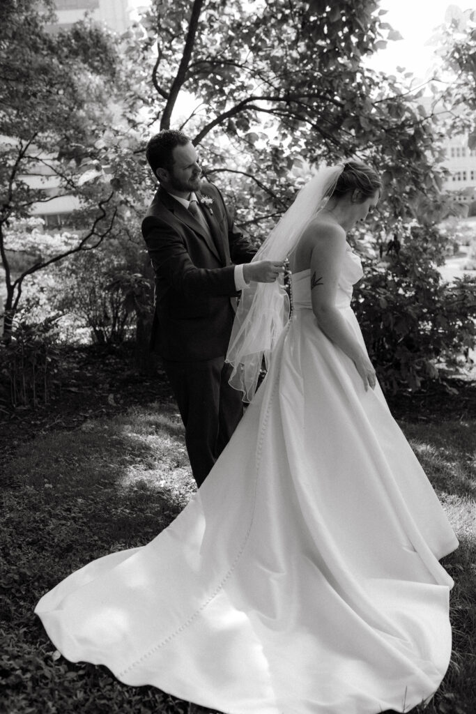 black and white candid wedding photo of groom fixing bride's veil; presence-driven storytelling